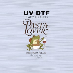 May include: A green frog wearing a red shirt is eating spaghetti and drinking wine. The text reads "UV DTF Ready to Apply Pasta Lover More Pasta Please The Kraft Shop By Kai".