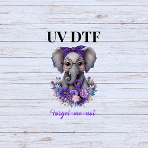 May include: A purple and gray elephant wearing glasses and a purple headband with white polka dots sits in a bed of purple and white flowers. The text "UV DTF" is above the elephant and the text "Forget-me-not" is below the elephant.