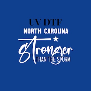 May include: White text on a blue background reads "UV DTF North Carolina Stronger Than The Storm" with a white star above the word "Stronger".