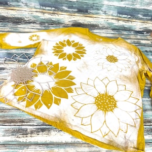 May include: A yellow long-sleeved shirt with a bleach-dye effect and a white sunflower design.