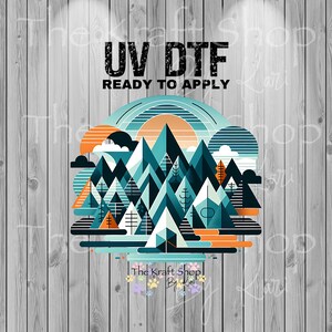 May include: A colorful graphic featuring a mountain range, trees, and a setting sun, with the text "UV DTF READY TO APPLY." The design uses shades of teal, orange, and white. The Kraft Shop By Kari logo is at the bottom.