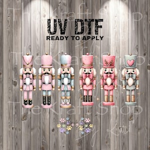 May include: A collection of six colorful nutcracker designs in pink, blue, and gold. Each nutcracker has a unique hat and uniform. The text "UV DTF READY TO APPLY" is displayed at the top. The Kraft Shop By Kari logo is at the bottom.