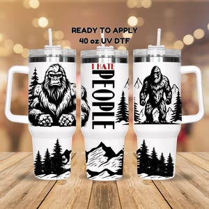 May include: White 40 oz UV DTF tumbler with a Bigfoot design. The design is black and white and features a Bigfoot, trees, and mountains. One tumbler has the text "I HATE PEOPLE". The tumblers have a handle and a straw.