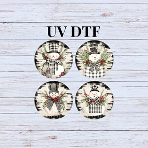 May include: Four round sublimation blanks with a black and white checkered pattern and a snowman design. The snowmen are wearing black top hats and black and white scarves. The snowmen are surrounded by greenery and red berries. The text "UV DTF" is printed at the top of the image.