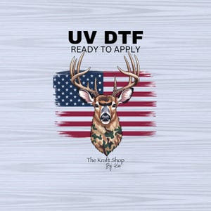 May include: UV DTF ready to apply graphic featuring a deer with large antlers, set against a stylized American flag. The deer has a camouflage pattern on its chest. The text "UV DTF READY TO APPLY" is at the top, and "The Kraft Shop By Kat" is at the bottom.