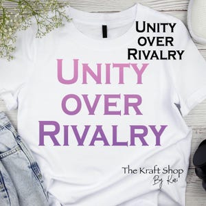 May include: White t-shirt with the words "UNITY OVER RIVALRY" in a gradient purple font. The text is stacked vertically. The Kraft Shop By Kari is printed at the bottom of the shirt.