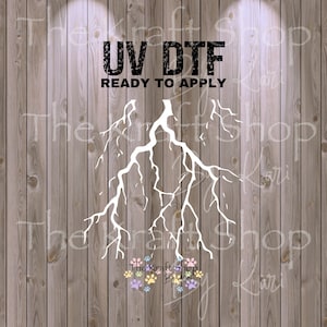 May include: A white lightning bolt design with the text "UV DTF READY TO APPLY" is displayed on a wooden background. The Kraft Shop logo is at the bottom. The design is suitable for various crafting projects.