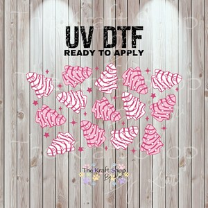May include: UV DTF ready to apply sheet featuring pink and white Christmas tree designs with star accents. The Kraft Shop By Kim logo is at the bottom. The background is a wood grain pattern.