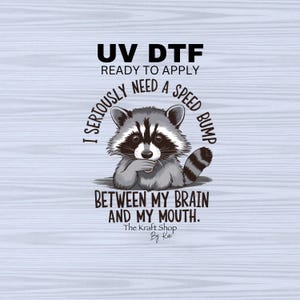May include: A raccoon with a mischievous expression is shown with the text "I seriously need a speed bump between my brain and my mouth." The text is in a circle around the raccoon. The text "UV DTF Ready to Apply" is at the top of the image. The text "The Kraft Shop By Ka" is at the bottom of the image.