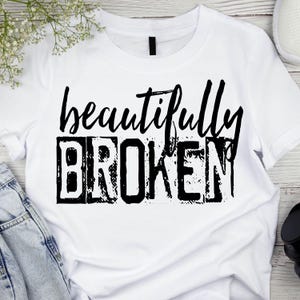 May include: White t-shirt with black text that reads "beautifully broken". The text has a distressed, vintage look.