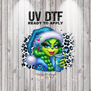 May include: A digital graphic featuring a green character with a blue Santa hat and a drink. The character has green hair, blue eyes, and red lipstick. The text "UV DTF READY TO APPLY" is at the top. The Kraft Shop By Kori logo is at the bottom.