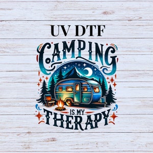 May include: A camping trailer with a campfire in front of it. The text "UV DTF CAMPING IS MY THERAPY" is written in a stylized font.