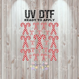 May include: UV DTF ready to apply transfer sheet featuring red and white candy canes. The design includes large and small candy canes arranged on a light wood grain background. The text "UV DTF READY TO APPLY" is at the top.