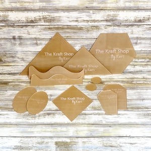 May include: A set of 11 acrylic craft stencils featuring various shapes, including a hexagon, a diamond, a wave, and circles. The stencils are beige and have the text "The Kraft Shop By Kari" printed on them.