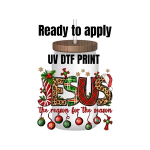 May include: A white tumbler with a wooden lid and a straw. The tumbler has a UV DTF print of the word "JESUS" in colorful letters with a Christmas theme. The text "the reason for the season" is printed below the word "JESUS".