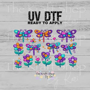 May include: A UV DTF ready to apply transfer sheet featuring colorful dragonfly and flower illustrations in purple, blue, orange, and pink. The designs include small skulls, hearts, and stars, with the text UV DTF READY TO APPLY at the top.
