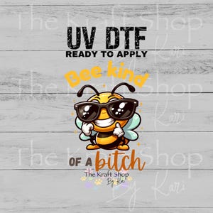 May include: A UV DTF transfer design featuring a cartoon bee wearing sunglasses and giving a thumbs up. The text reads "Bee kind of a bitch" and "Ready to Apply". The design is on a light gray wood grain background.