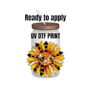 May include: A white tumbler with a wooden lid and a straw. The tumbler has a sunflower with bees and honeycomb design and the text "UV DTF PRINT" printed on it. The text "Ready to apply" is above the tumbler.