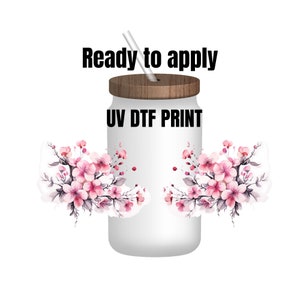 May include: A white glass tumbler with a wooden lid and a straw. The tumbler is decorated with pink cherry blossom floral designs and the text "Ready to apply" and "UV DTF PRINT" in black.