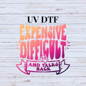 May include: A graphic design with the text "UV DTF Expensive Difficult and Talks Back" in pink and orange lettering on a white wood background.
