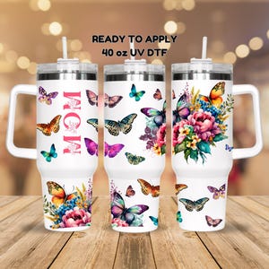 May include: White 40 oz tumbler with a handle and a straw. The tumbler has a design of colorful butterflies and flowers with the word "MOM" in pink lettering. The tumbler is ready to apply UV DTF.
