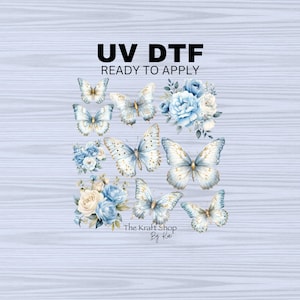 May include: A set of blue and white butterfly and flower iron-on transfers. The transfers are ready to apply and are labeled "UV DTF". The text "The Kraft Shop By Kai" is also included in the image.