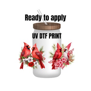 May include: A white tumbler with a wooden lid and a straw. The tumbler has a red cardinal design with flowers and greenery. The text "UV DTF PRINT" is printed on the tumbler. The text "Ready to apply" is printed above the tumbler.