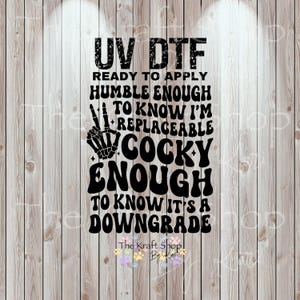 May include: Black UV DTF transfer with the text "UV DTF READY TO APPLY HUMBLE ENOUGH TO KNOW I'M REPLACEABLE COCKY ENOUGH TO KNOW IT'S A DOWNGRADE". The image includes a skeleton hand making a peace sign.