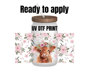 May include: A white tumbler with a wooden lid and a straw. The tumbler has a floral pattern and a picture of a Highland cow with a flower crown. The text "UV DTF PRINT" is printed on the tumbler.