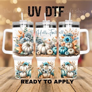 May include: Three white insulated tumblers with handles, decorated with watercolor pumpkins, blue flowers, and fall foliage. The text "Hello Fall" is displayed on the center tumbler. The bottom of the tumblers read "READY TO APPLY".