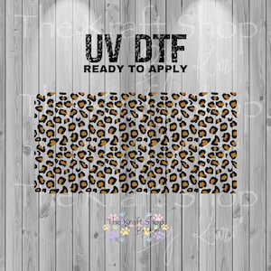 May include: UV DTF ready to apply sheet featuring a leopard print pattern. The design includes black and gold spots on a white background. The text "UV DTF READY TO APPLY" is displayed in black, with the shop's logo at the bottom.