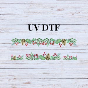 May include: Two rows of green holly sprigs with red berries and gold pine cones on a white wood background. The text "UV DTF" is printed above the sprigs.