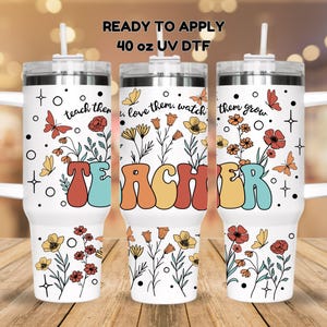May include: Three 40 ounce stainless steel tumblers with a white background and floral designs. The tumblers have a handle and a straw. The text "teach them, love them, watch them grow" and "TEACHER" are printed on the tumblers.