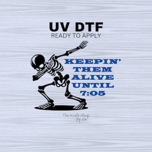 May include: A skeleton in a dabbing pose with the text "Keepin' Them Alive Until 7:05" in blue. The text "UV DTF Ready to Apply" is at the top of the image. The text "The Kraft Shop By Kai" is at the bottom of the image.