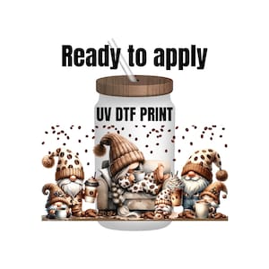 May include: A white tumbler with a brown lid and a straw. The tumbler has a UV DTF print of four gnomes with coffee cups and coffee beans. The text "UV DTF PRINT" is printed on the tumbler.