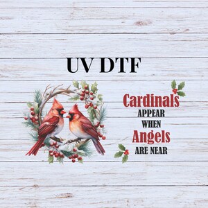 May include: UV DTF design featuring two red cardinals perched on a wreath with red berries and snow. The text reads "Cardinals appear when angels are near".