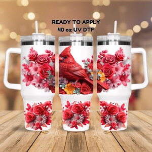 May include: Three 40 ounce white stainless steel tumblers with lids and handles. The tumblers are decorated with a red cardinal bird and pink and white flowers. The text "READY TO APPLY 40 oz UV DTF" is printed on the top of the image.