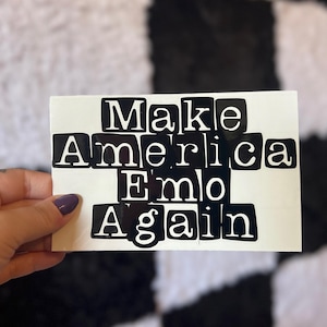 May include: Black and white sticker with the text "Make America Emo Again" in a blocky font.