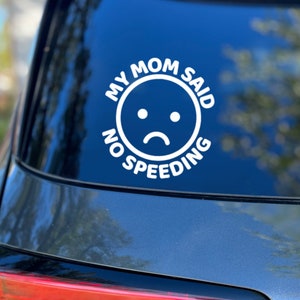 Op de afbeelding: Witte vinyl auto sticker met de tekst "My Mom Said No Speeding" en een emoji met een verdrietig gezicht.