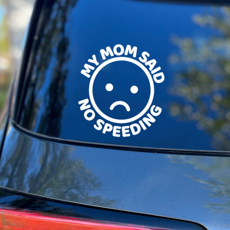 Op de afbeelding: Witte vinyl auto sticker met de tekst "My Mom Said No Speeding" en een emoji met een verdrietig gezicht.