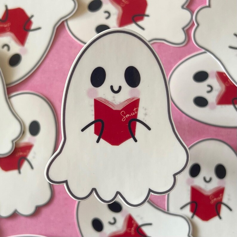 May include: A white ghost with a friendly face is reading a red book with the word "Smut" written on the cover. The ghost is holding the book with its hands and has a happy expression on its face.