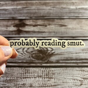 Puede incluir: Una pegatina blanca con texto negro que dice "probably reading smut."