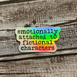 May include: A rainbow holographic sticker with the text "emotionally attached to fictional characters".