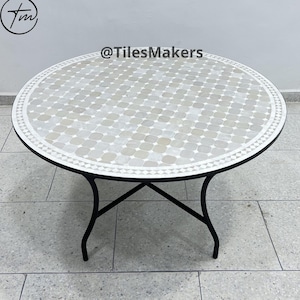 Pode incluir: Uma mesa redonda de mosaico de azulejos brancos e cinzentos com uma estrutura de metal preto. A mesa está sobre um piso de ladrilhos cinzentos. O texto "@TilesMakers" é visível na imagem.