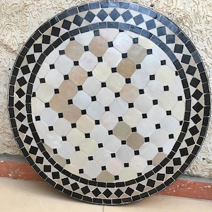 May include: Round black and white mosaic table top with a geometric pattern. The table top is made of small tiles arranged in a repeating pattern of diamonds and octagons.