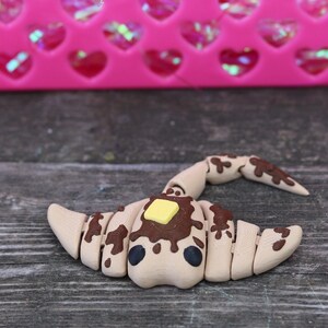 May include: A brown and tan segmented stingray figurine with a yellow square on top, resembling a pat of butter. The figurine is on a woodgrain surface.