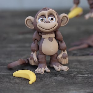 May include: A brown monkey figurine with a big smile and a banana. The monkey has articulated arms and legs.