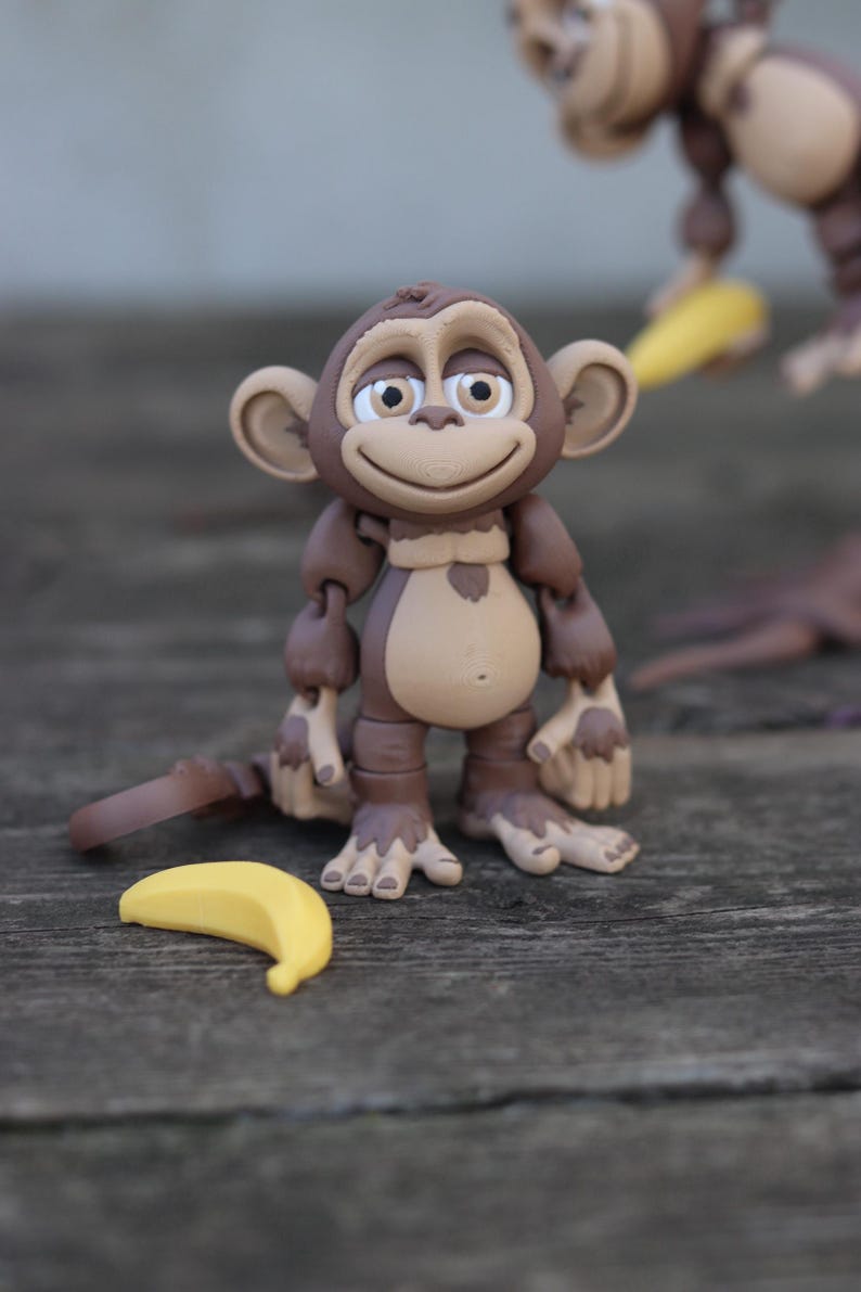 May include: A brown monkey figurine with a big smile and a banana. The monkey has articulated arms and legs.
