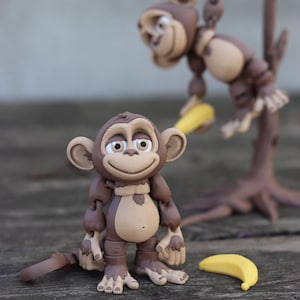 May include: Two brown monkey figurines, one standing and one hanging from a tree branch. The standing monkey is holding a yellow banana in its hand. The hanging monkey is holding a yellow banana in its mouth. Both monkeys have brown fur and black eyes.
