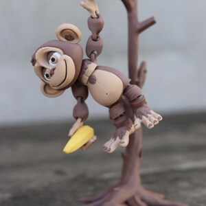 May include: A brown monkey figurine holding a yellow banana, hanging from a brown tree branch with a brown base.